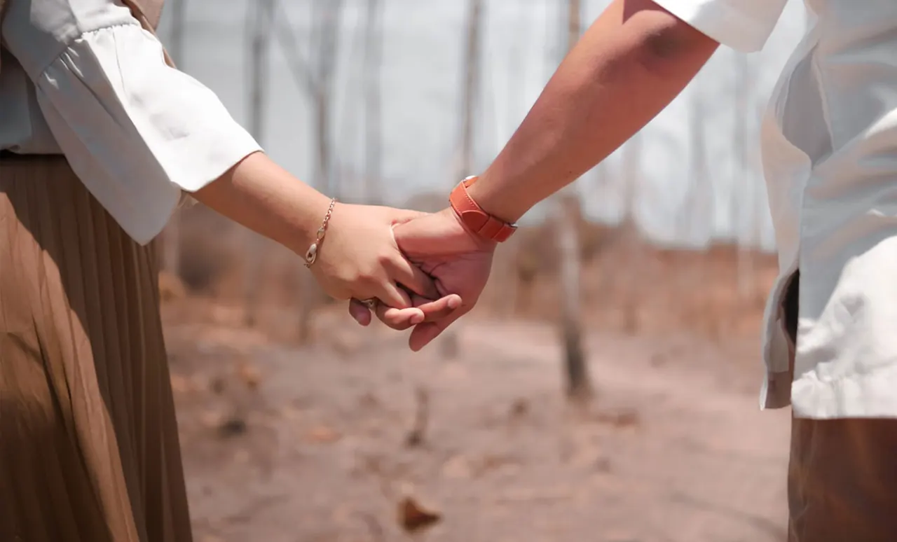 Two people holding hands on a woodland path